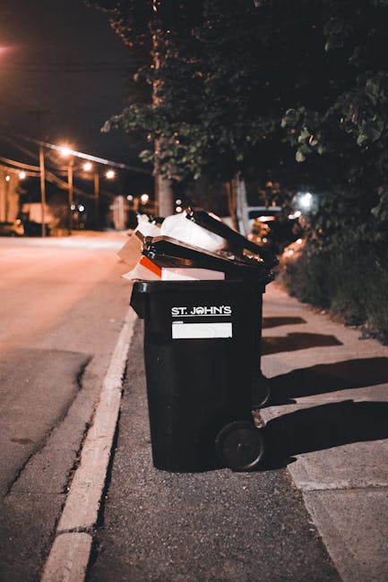 The image shows a person disposing of brown paper bags into a white waste bin that has a black interior, likely used for rubbish collection. The person's arm, clad in a short sleeve, extends diagonall